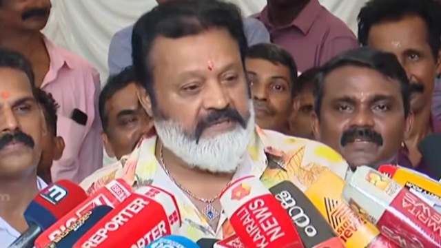 Suresh Gopi speaking to reporters surrounded by microphones from Kerala news channels