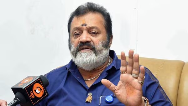 Suresh Gopi seated, gesturing while speaking to a reporter holding a microphone
