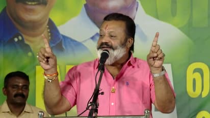 Suresh Gopi speaking at a lectern with both hands raised while addressing a gathering