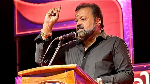 Suresh Gopi speaking from a lectern on a stage, one hand raised